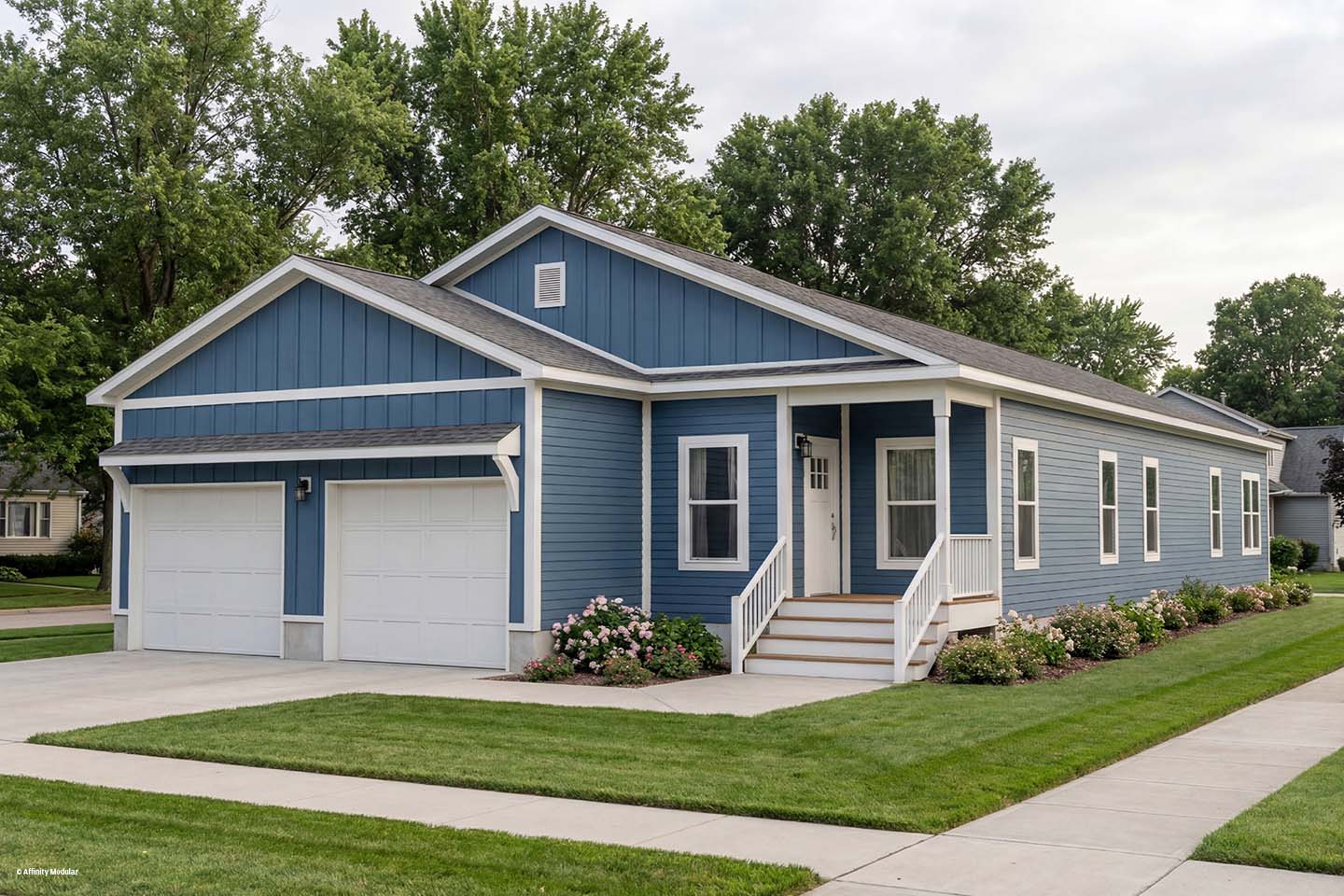 A blue single-story modular home with white trim, a front porch, and a two-car garage, surrounded by green lawn.